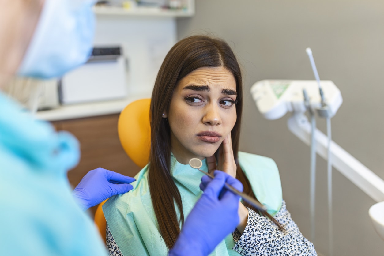 A woman expressing oral pain in a dentist's office