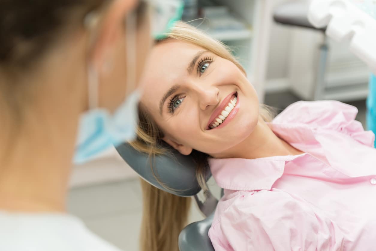 Horizontal color close-up headshot of beautiful woman having dental examination and sincerely smiling at dentist.